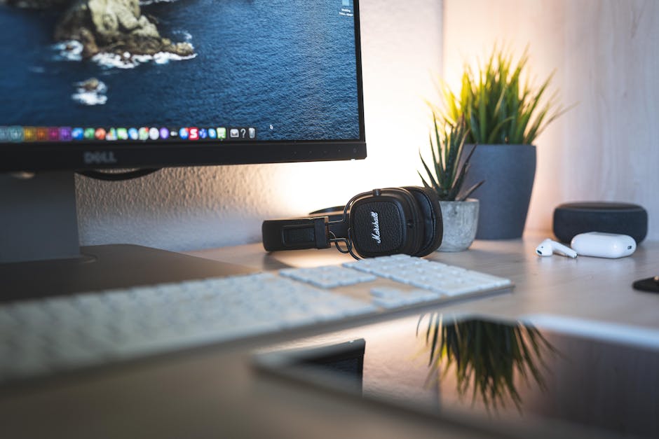 A minimalistic desk setup featuring a monitor, headphones, keyboard, and green plants.